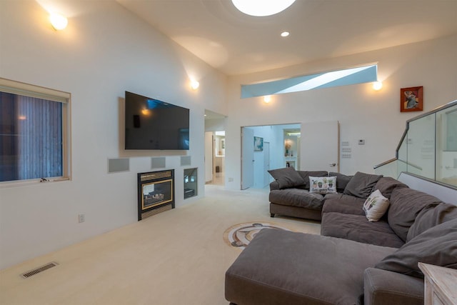 living room featuring visible vents, stairway, a glass covered fireplace, carpet flooring, and high vaulted ceiling