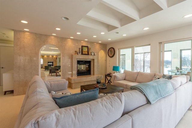 carpeted living area featuring arched walkways, beam ceiling, recessed lighting, a tiled fireplace, and coffered ceiling