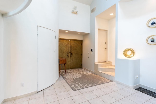 foyer with light tile patterned floors, baseboards, a high ceiling, and visible vents