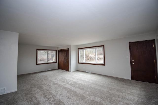 carpeted spare room with a healthy amount of sunlight, visible vents, and baseboards