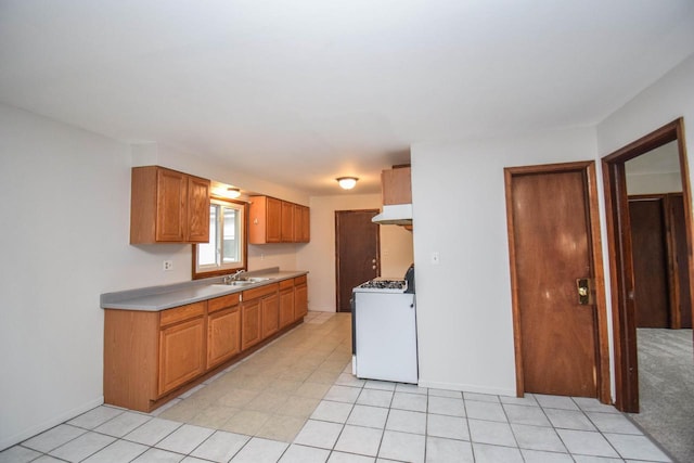 kitchen with baseboards, brown cabinetry, white gas range, under cabinet range hood, and a sink