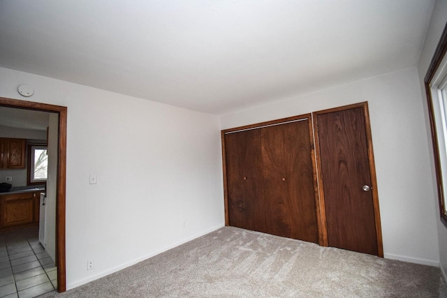 unfurnished bedroom with light carpet, light tile patterned floors, a closet, and baseboards