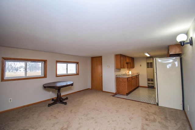 kitchen featuring light carpet, baseboards, brown cabinets, light countertops, and a sink