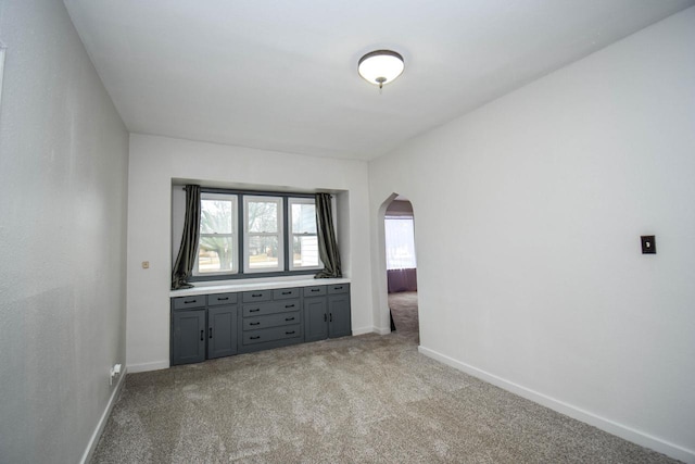 spare room featuring baseboards, arched walkways, and carpet flooring