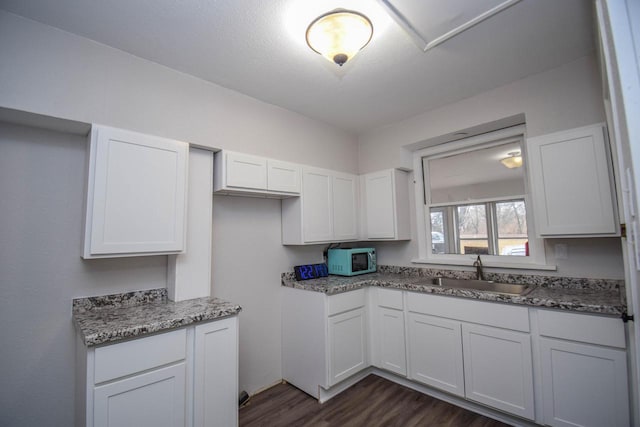 kitchen with dark wood finished floors, white microwave, a sink, and white cabinetry