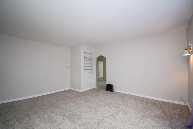 empty room with arched walkways, carpet, visible vents, and baseboards