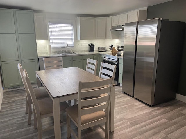 kitchen featuring stainless steel appliances, backsplash, a sink, light wood-type flooring, and under cabinet range hood