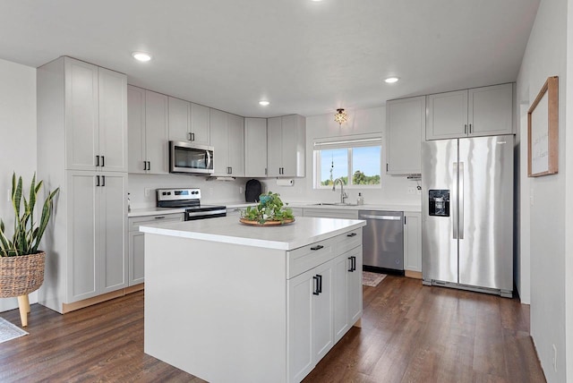 kitchen with dark wood finished floors, light countertops, appliances with stainless steel finishes, a sink, and a kitchen island