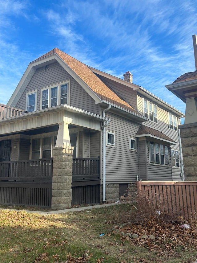 view of side of home featuring covered porch, a shingled roof, and a chimney