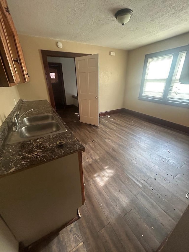 kitchen featuring a textured ceiling, dark wood-type flooring, a sink, baseboards, and brown cabinets