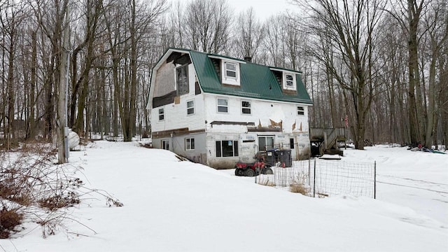 snow covered property with stone siding, a barn, and a gambrel roof