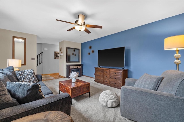 living room with ceiling fan, a fireplace, baseboards, stairs, and carpet