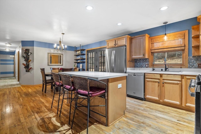 kitchen featuring decorative backsplash, appliances with stainless steel finishes, light wood-style floors, a sink, and a kitchen island