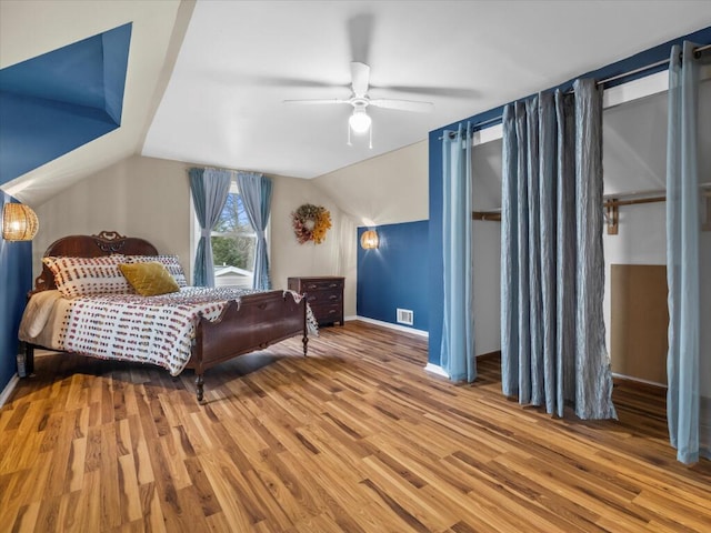 bedroom featuring a ceiling fan, visible vents, vaulted ceiling, and wood finished floors