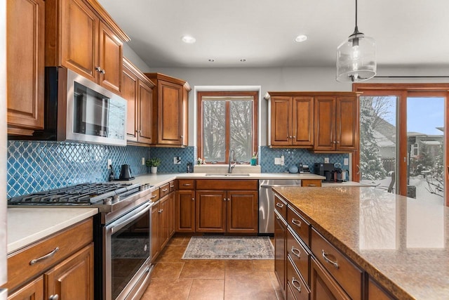 kitchen featuring pendant lighting, stainless steel appliances, tasteful backsplash, brown cabinetry, and a sink