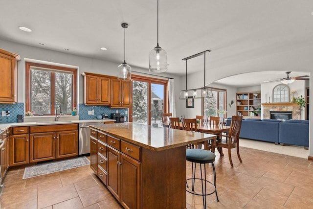 kitchen with brown cabinetry, dishwasher, a breakfast bar, decorative light fixtures, and a sink