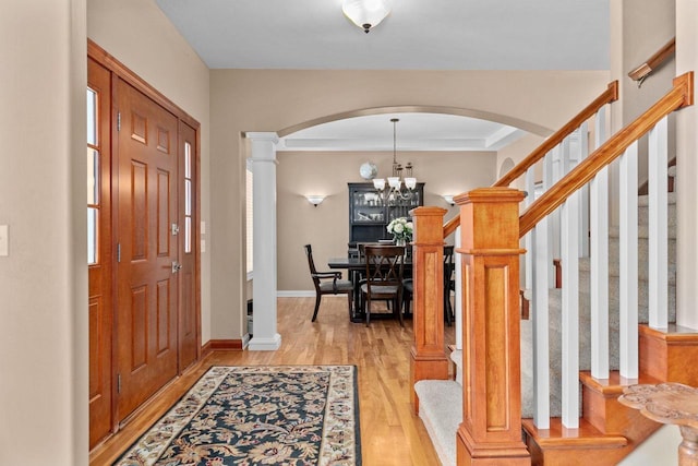 entryway featuring arched walkways, baseboards, light wood-style floors, stairway, and decorative columns