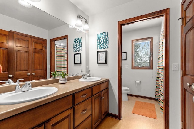 bathroom featuring baseboards, a sink, toilet, and double vanity