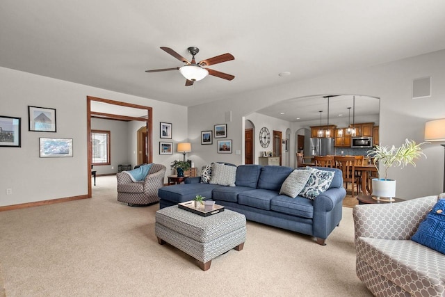 living room featuring arched walkways, baseboards, a ceiling fan, and light colored carpet