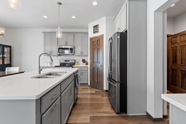 kitchen with decorative backsplash, appliances with stainless steel finishes, light countertops, gray cabinetry, and a sink