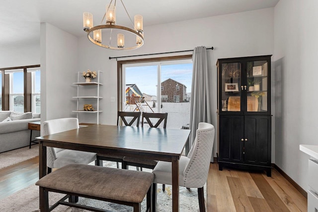 dining space with light wood-type flooring, an inviting chandelier, and baseboards