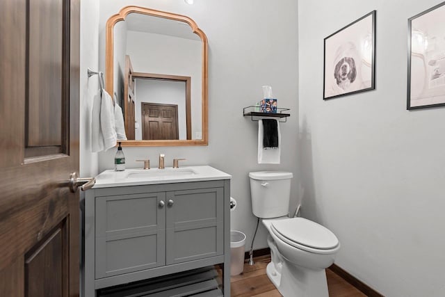 half bathroom with toilet, wood finished floors, vanity, and baseboards