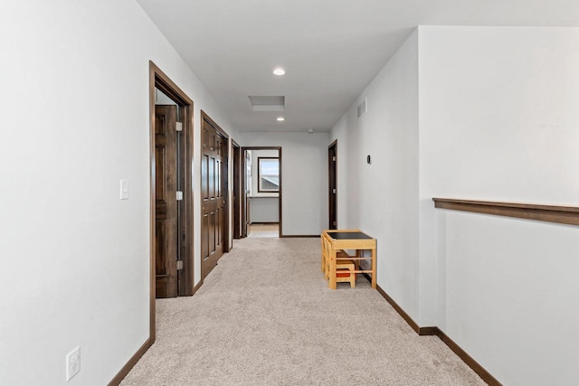 hall featuring light carpet, baseboards, visible vents, and attic access