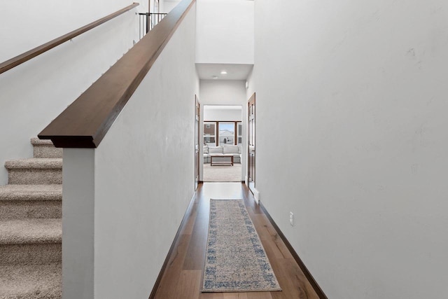 hallway with a towering ceiling, baseboards, stairway, and wood finished floors