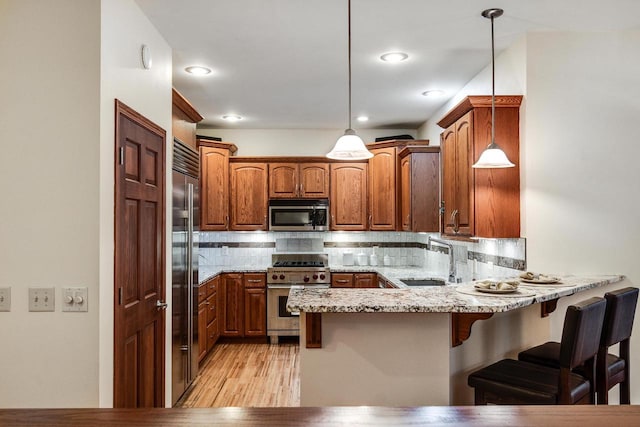 kitchen featuring backsplash, a sink, light stone countertops, high quality appliances, and a peninsula