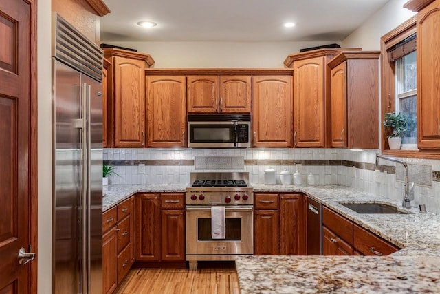 kitchen featuring light stone counters, backsplash, light wood-style floors, a sink, and high quality appliances