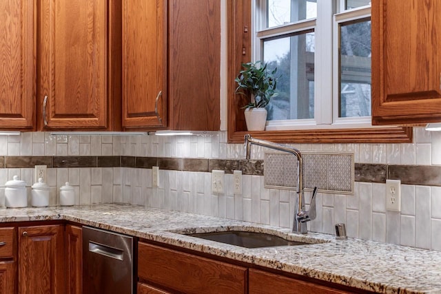 kitchen featuring backsplash, a sink, light stone countertops, and brown cabinets