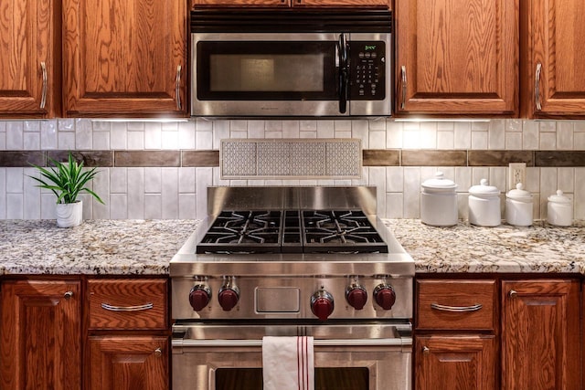 kitchen featuring stainless steel appliances, brown cabinetry, backsplash, and light stone countertops