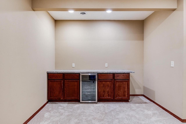 bar featuring light carpet, beverage cooler, baseboards, and a bar