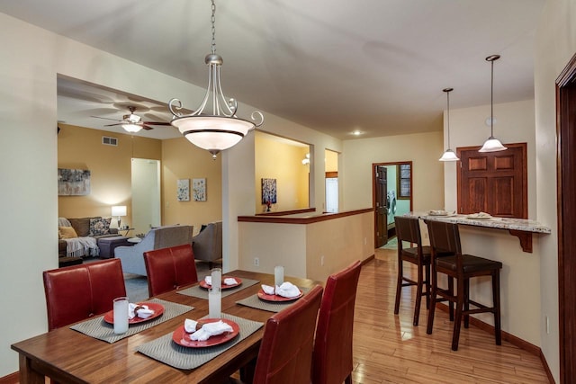 dining space featuring baseboards, visible vents, ceiling fan, and light wood finished floors