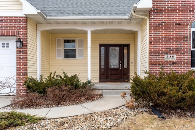 view of exterior entry featuring a shingled roof, brick siding, and a garage