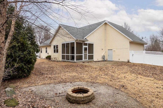 rear view of house featuring an outdoor fire pit, fence, and a sunroom