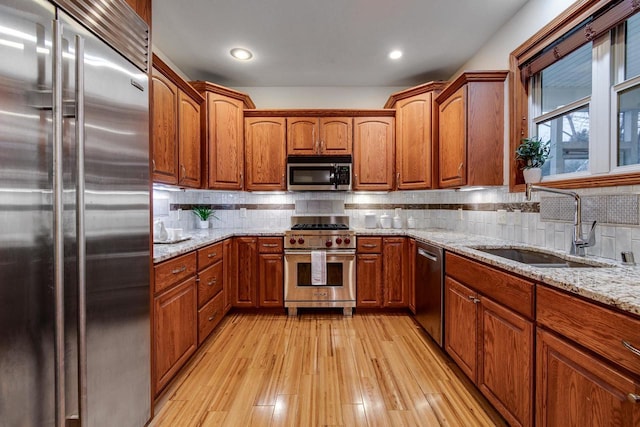 kitchen featuring light wood-type flooring, brown cabinets, a sink, and high quality appliances