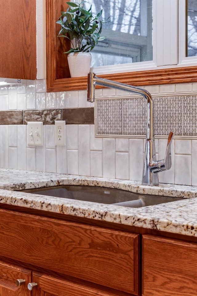 interior details with light stone countertops, backsplash, brown cabinetry, and a sink