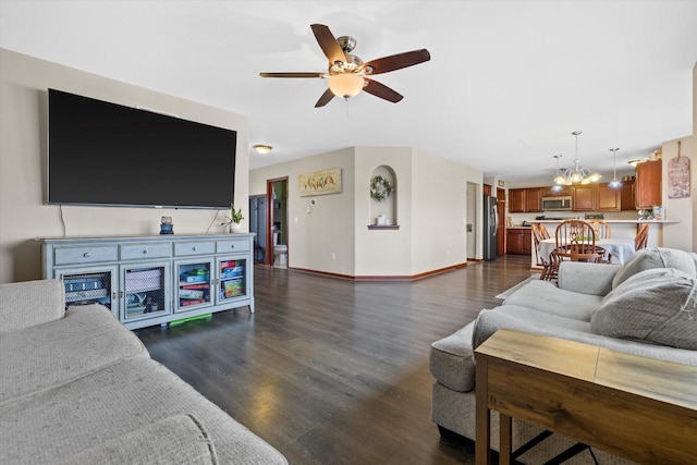 living area featuring dark wood-style floors, ceiling fan with notable chandelier, and baseboards