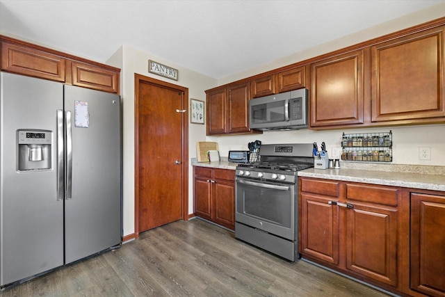 kitchen with brown cabinets, appliances with stainless steel finishes, light countertops, and dark wood-style flooring