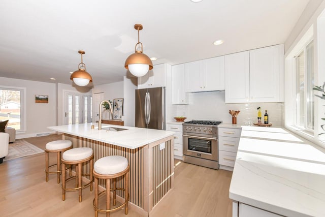 kitchen with a sink, white cabinetry, light wood-style floors, appliances with stainless steel finishes, and backsplash