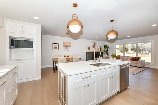 kitchen featuring light wood-style flooring, a sink, open floor plan, appliances with stainless steel finishes, and pendant lighting