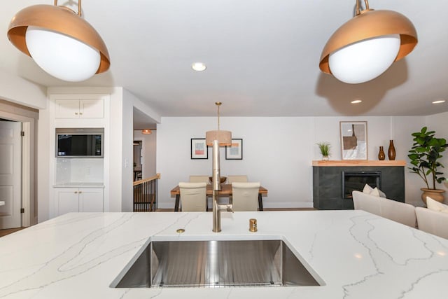 kitchen with light stone counters, decorative light fixtures, a fireplace, recessed lighting, and a sink