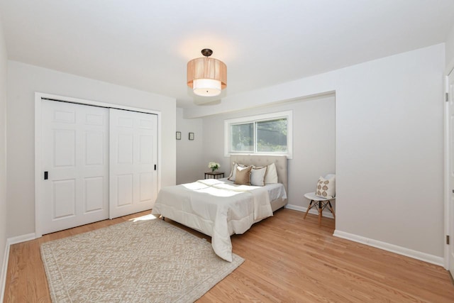 bedroom with light wood-style flooring, baseboards, and a closet