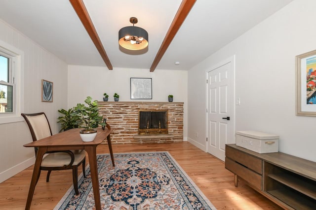 office with a fireplace with raised hearth, beamed ceiling, light wood-type flooring, and baseboards