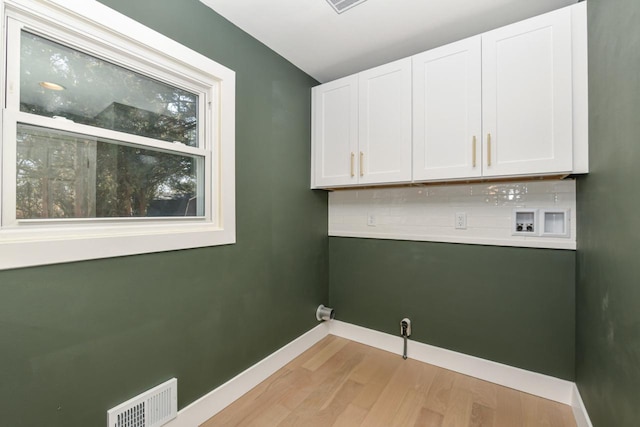 clothes washing area featuring washer hookup, visible vents, light wood-style floors, baseboards, and cabinet space