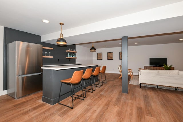 kitchen featuring a breakfast bar, decorative light fixtures, light wood finished floors, light countertops, and freestanding refrigerator