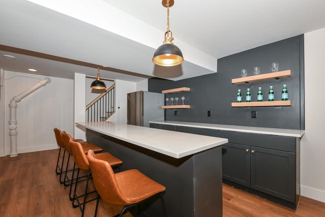 bar featuring wood finished floors, stairway, freestanding refrigerator, indoor wet bar, and pendant lighting