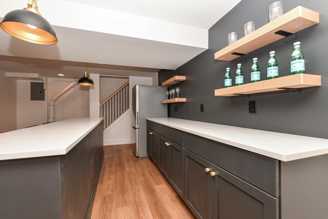 bar featuring electric panel, decorative light fixtures, freestanding refrigerator, stairs, and light wood-style floors