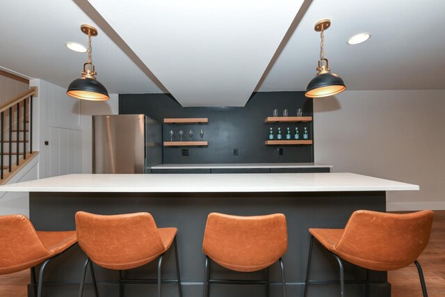 bar with pendant lighting, freestanding refrigerator, wood finished floors, bar, and stairs